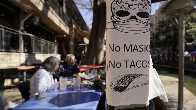 A sign requiring make is seen near diners eating at a restaurant on the River Walk,