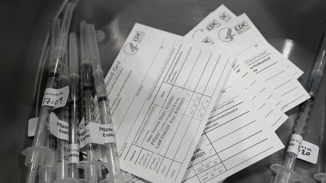 Syringes with doses of the Pfizer COVID-19 vaccine, are shown next to vaccination cards,