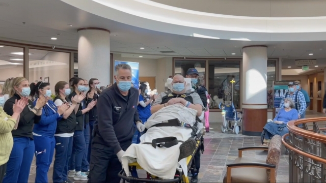 Nurses clap as man is wheeled out of the hospital.
