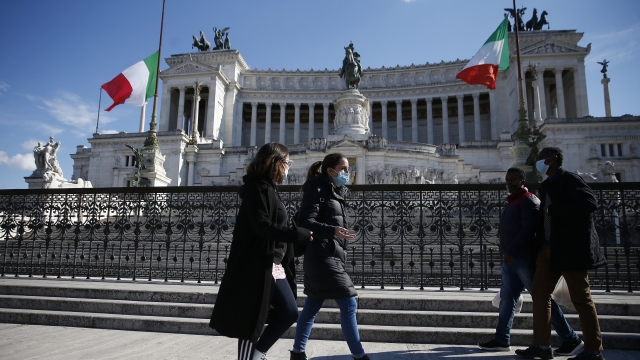 People walk past a monument as flags fly at half-staff on a national day of mourning for Italy's COVID-19 death