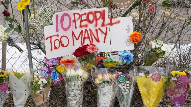 A sign stands above floral bouquets lined along the temporary fence around a King Soopers grocery store.