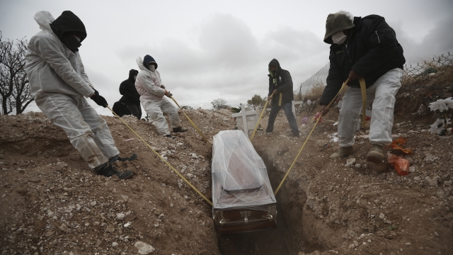 Workers wearing full protection gear amid the new coronavirus pandemic, lower a coffin into a grave.