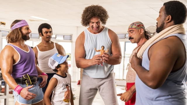 Andre the Giant, portrayed by actor Matthew Willig, shows action figure to wrestler friends.