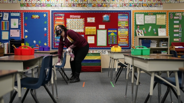 A teacher cleans a desk in a classroom.