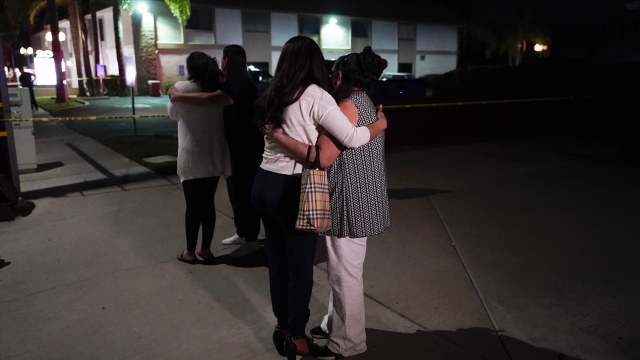 Unidentified people comfort each other as they stand near a business building where a shooting occurred in Orange, Calif.