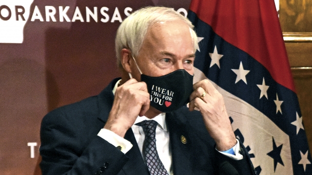 Arkansas Gov. Asa Hutchinson removes his mask before a briefing at the state capitol in Little Rock.