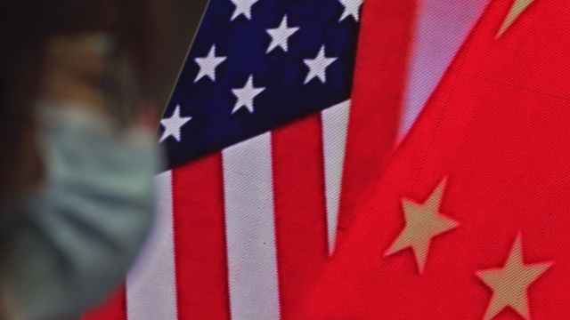 A woman sits near a screen showing China and U.S. flags