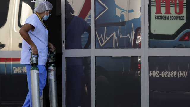 A health care worker carries oxygen tanks into an area designated for the treatment of COVID-19.