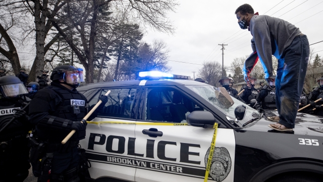 A man stands atop a police car after throwing a brick at the windshield near the site of a shooting.