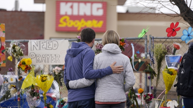 Mourners walk the temporary fence line outside the parking lot of a King Soopers grocery store
