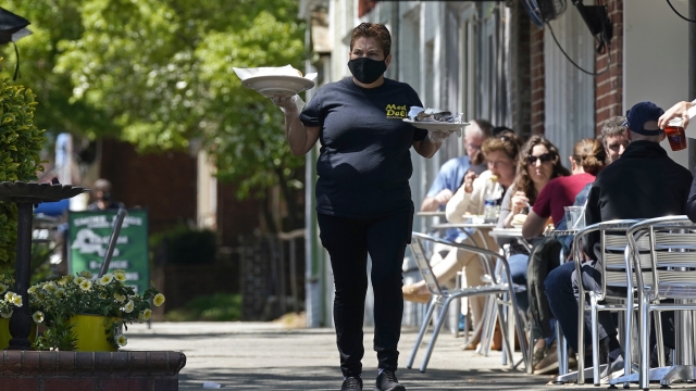 A member of the wait staff delivers food to outdoor diners along the sidewalk at the Mediterranean Deli