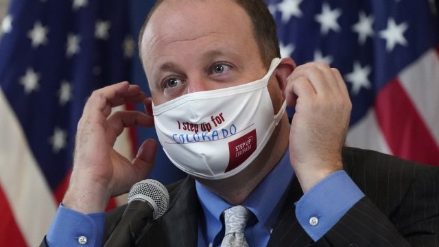 Colorado Governor Jared Polis adjusts his face covering.