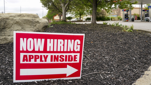 A "Now Hiring" sign posted outside and American business.