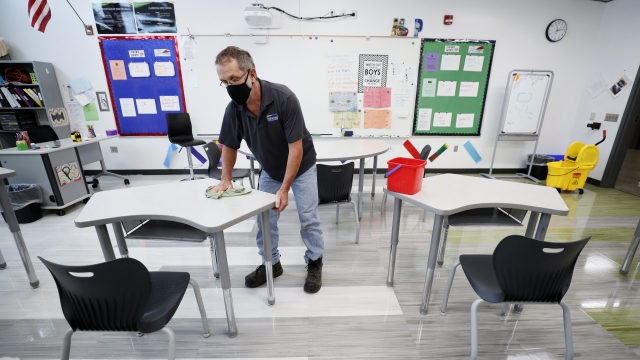 Custodian wiping down desks in an empty classroom.