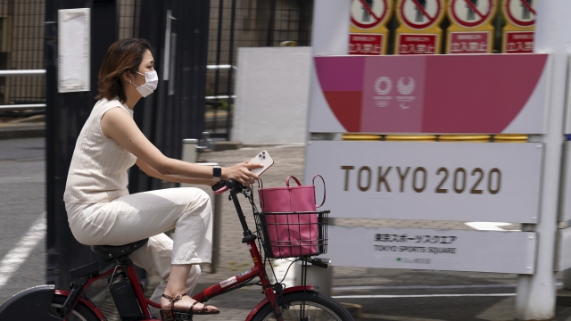 A woman wearing a protective mask rides past a a banner for the Tokyo 2020 Olympic and Paralympic Games in Tokyo, Japan