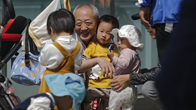 An elderly man plays with children near a commercial office building in Beijing, China