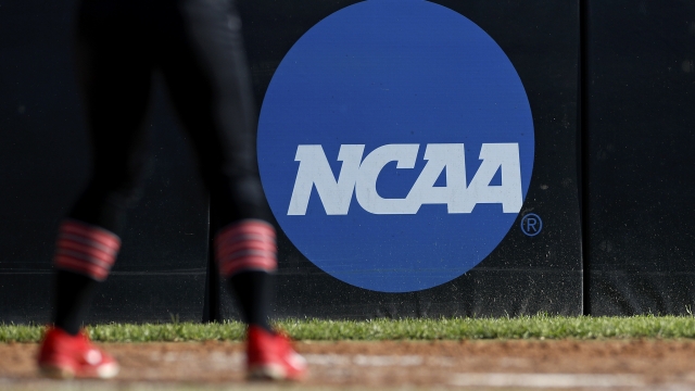 College athlete stands near the NCAA logo during a softball game.