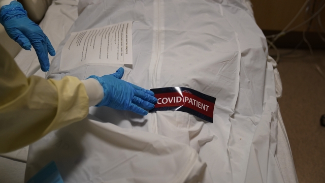 A hospital worker places a "COVID Patient" sticker on a body bag holding a deceased patient