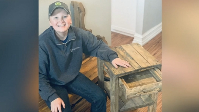 Boy sits next to a wooden nightstand