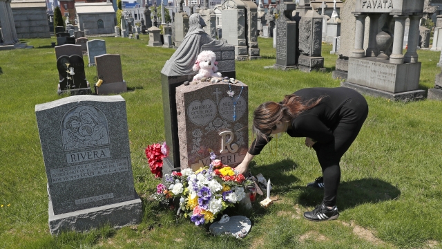 Sharon Rivera adjusts flowers and other items left at the grave of her daughter, Victoria, at Calvary Cemetery in New York.