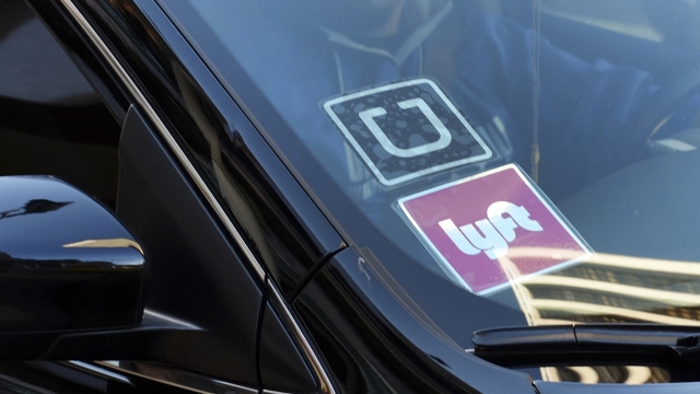 A ride share car displays Lyft and Uber stickers on its front windshield