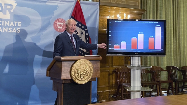 Arkansas Gov. Asa Hutchinson stands next to a chart displaying COVID-19 hospitalization