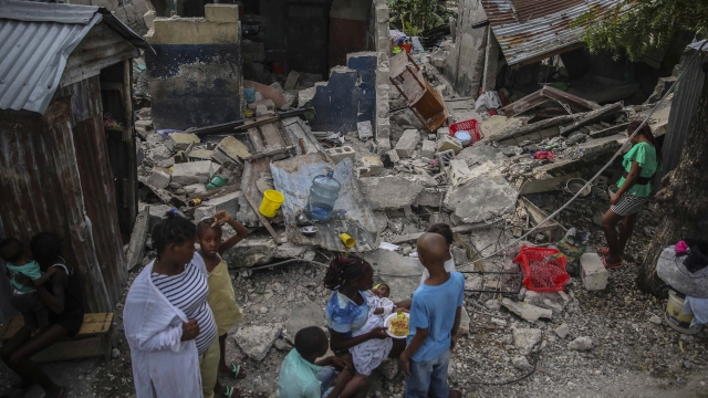 A family eats breakfast in front of homes destroyed by a 7.2 magnitude earthquake in Les Cayes, Haiti