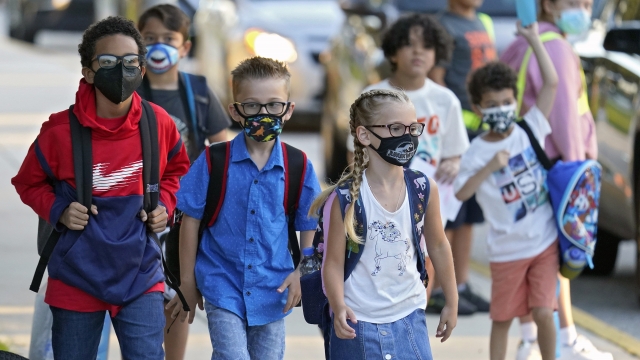 Students, some wearing protective masks, arrive for the first day of school.