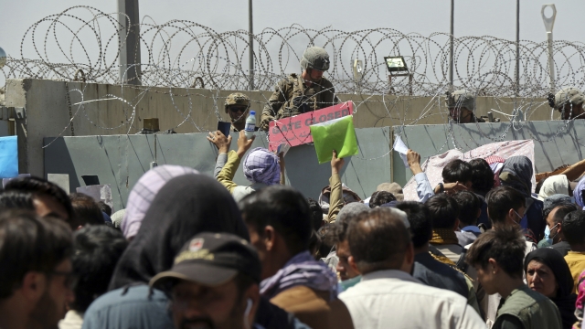 A U.S. soldier holds a sign as hundreds of people gather near an evacuation control checkpoint