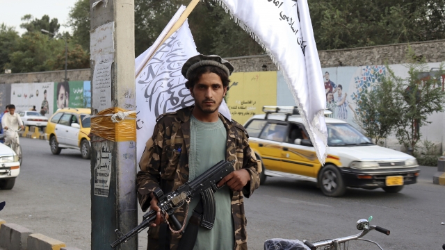 A Taliban fighter holds his weapon under Taliban flags hanging on a street in Kabul, Afghanistan.