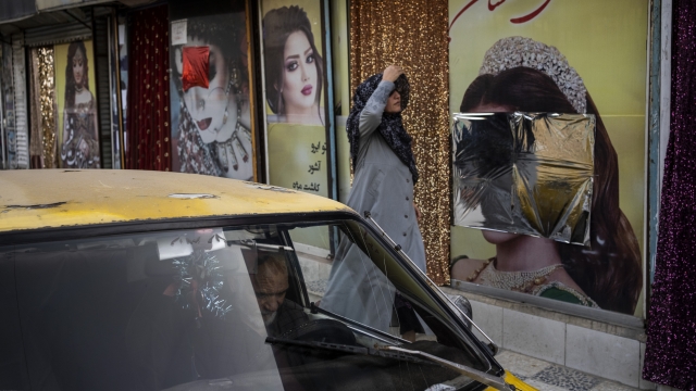 An Afghan woman walks past beauty salons with defaced window decorations