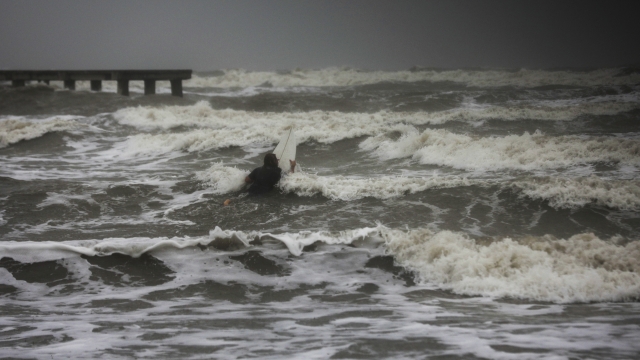 A surfer tries to paddle through the surf as wind and rain from Tropical Storm Nicholas batters the area.