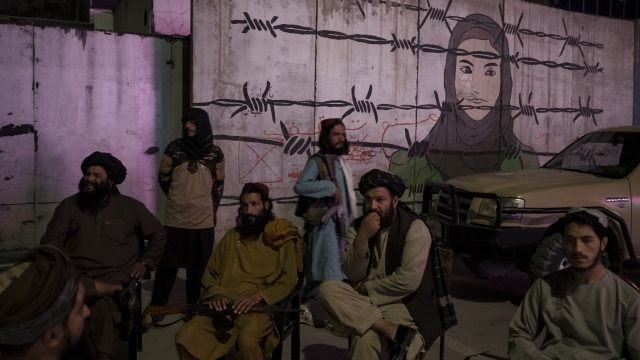 Taliban members sit in front of a mural depicting a woman behind barbed wire