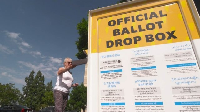 Woman drops an envelope into a ballot box.
