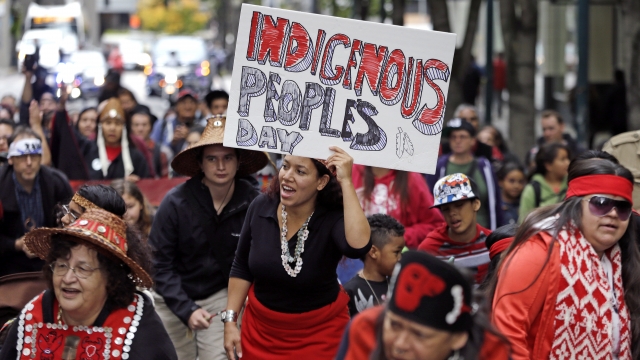 A woman holds a sign for Indigenous Peoples Day during a demonstration and march