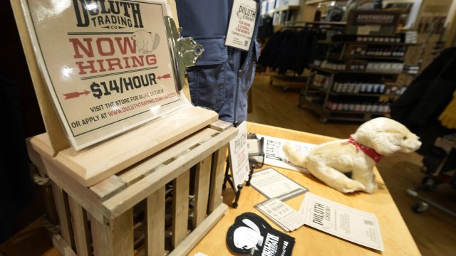 A now hiring sign sits on a display in a clothing store