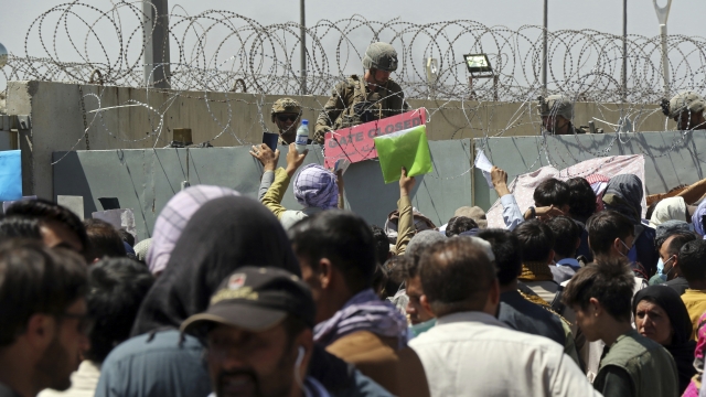 A U.S. soldier holds a sign indicating a gate is closed as hundreds of people gather at the Airport in Kabul, Afghanistan.