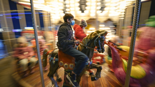 Children wearing face masks enjoy a carousel ride