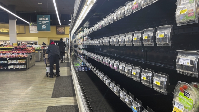 Shoppers walk past empty aisles of produce