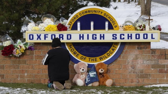 A well wisher kneels at a memorial on the sign of Oxford High School