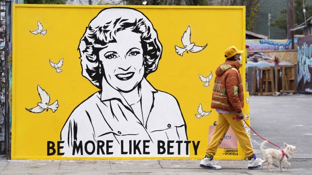 A man walks a dog past a new mural of the late actress Betty White by artist Corie Mattie