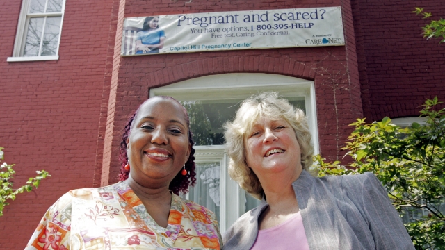 Two women stand in front of an abortion sign.