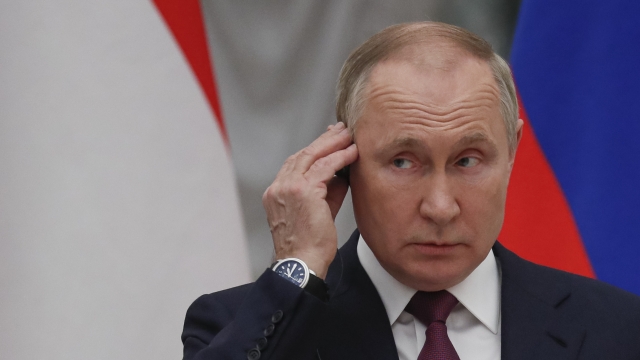Russian President Vladimir Putin touches his earpiece during a conference.