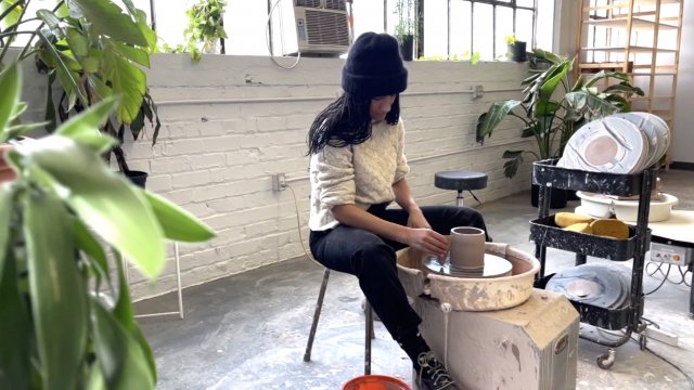 A woman sits sculpting pottery.