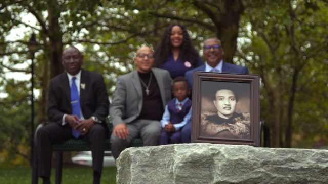The Lacks family and their attorney sit behind a photo of Henrietta Lacks.