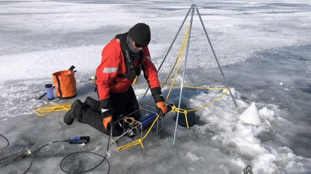 Scientist cuts a hole in ice to sample lake water