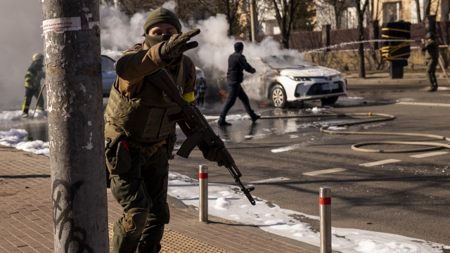 Ukrainian soldiers take positions outside a military facility as two cars burn, in a street in Kyiv