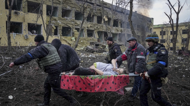 Ukrainian emergency employees and volunteers carry an injured pregnant woman from a hospital building damaged by shelling
