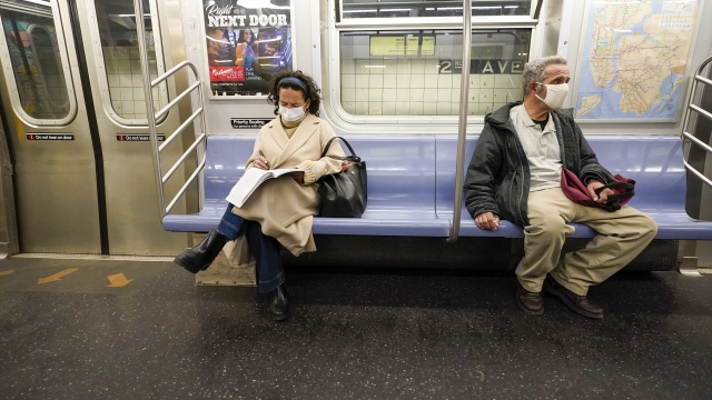 Commuters wear face masks and social distance while riding the subway.