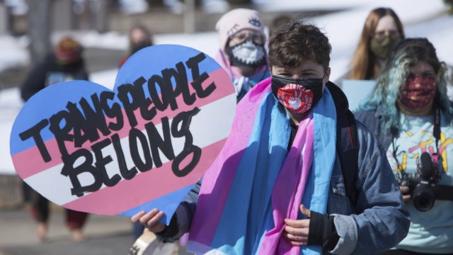 A person marches with a 'Trans People Belong' sign